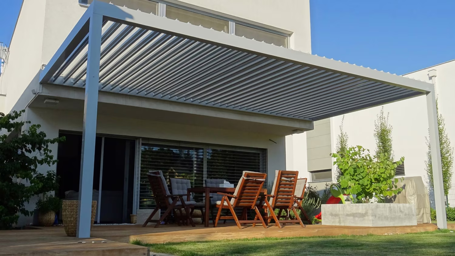 Bioklimatikus alumínium pergola állítható lamellákkal terasz fölött étkezőgarnitúrával modern ház mellett