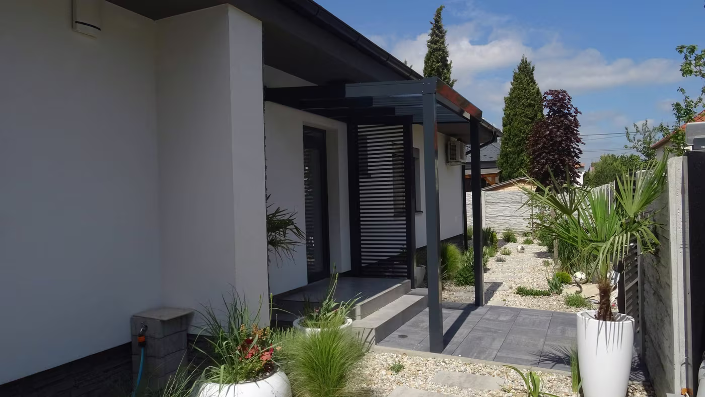 Antracit Economic Class alumínium pergola fehér ház mentén cserepes növényekkel