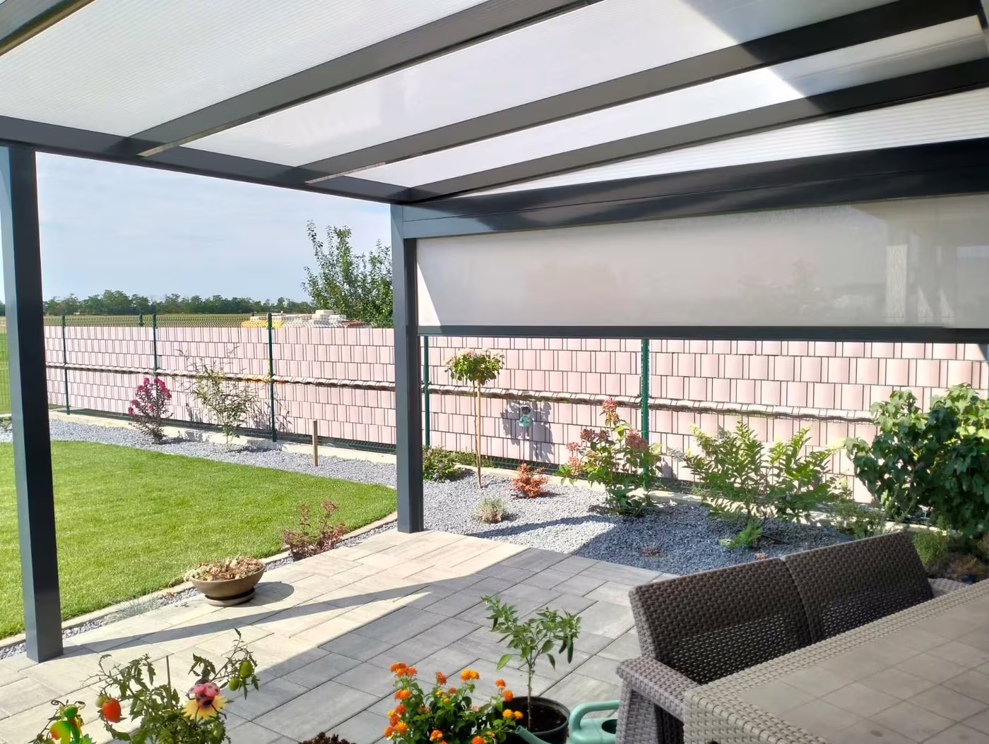 Antracit Economic Class alumínium pergola kerítés mentén rattan ülőgarnitúrával és virágokkal